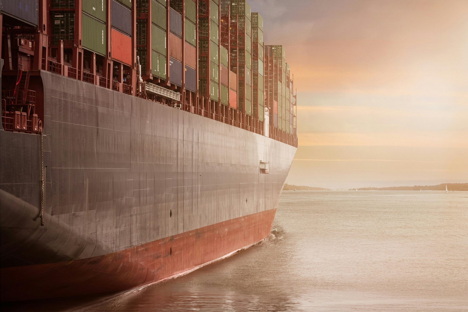 pexels-photo-262353-262353 A colossal cargo ship loaded with containers navigates through calm waters against a vibrant sunset sky.
