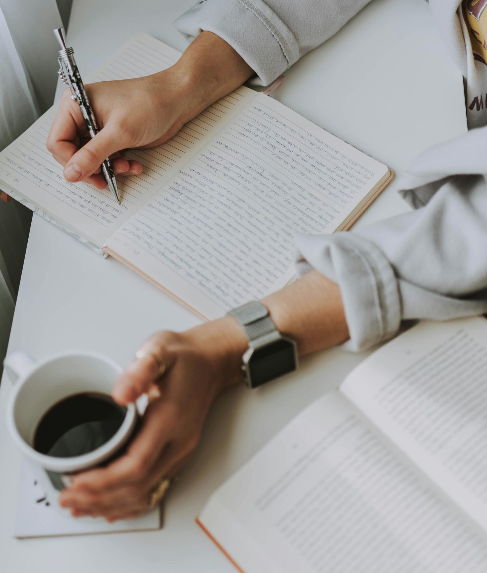 pexels-photo-3278757-3278757 Close-up of a person writing in a notebook with coffee on a desk. Ideal for workplace or study themes.